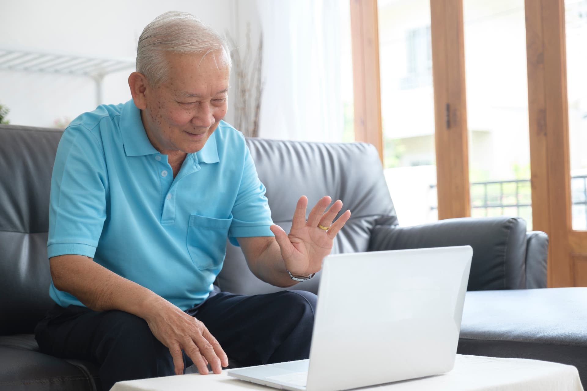 An older man waving warmly during a video call on a laptop at home