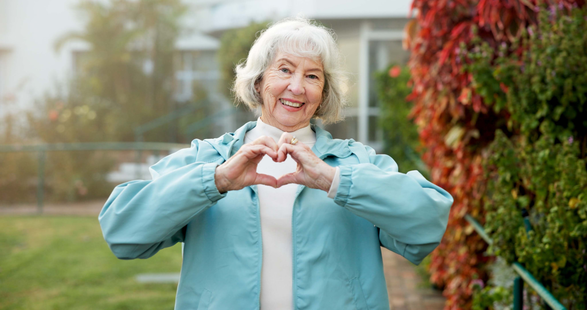 A cheerful older woman outdoors making a heart shape with her hands